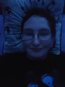 Danni is lying in bed and smiling. The image has a dark blueish hue. 